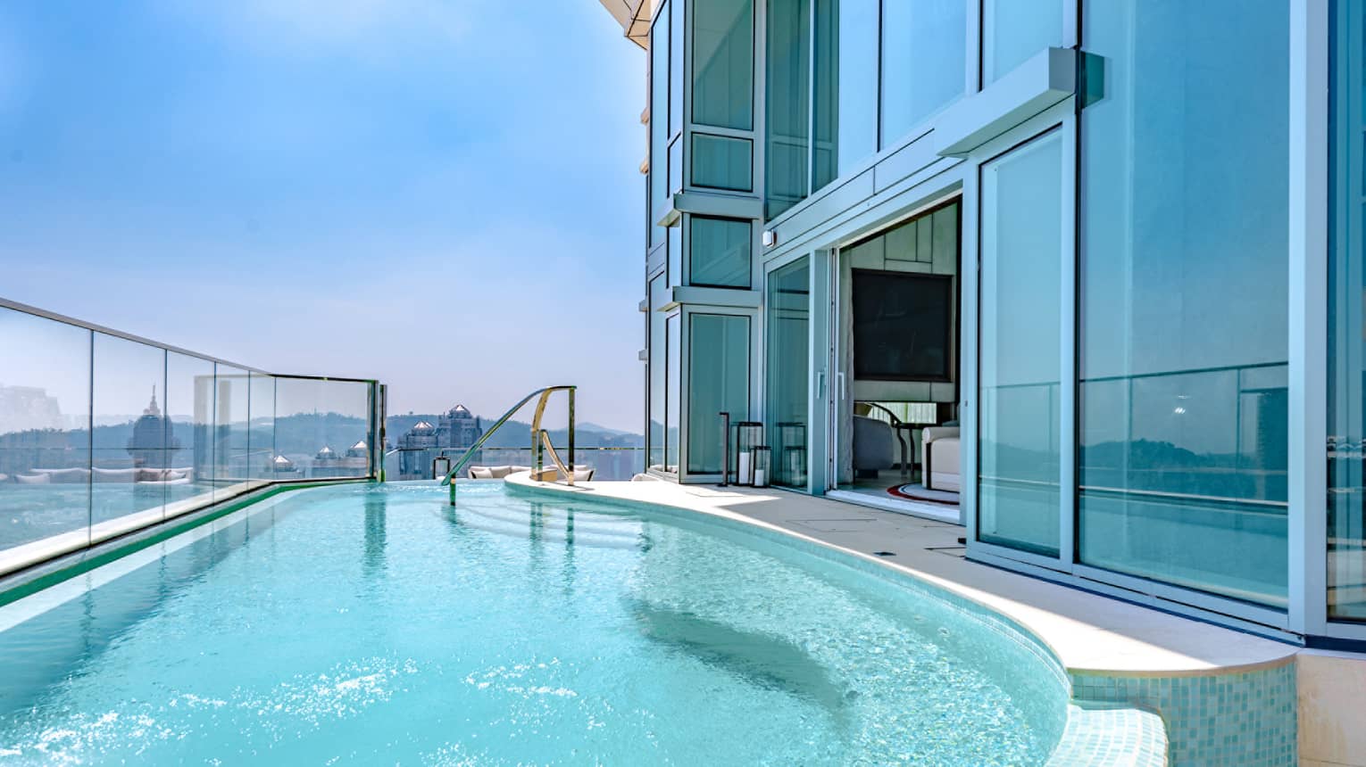 Sliding glass doors leading onto an expansive outdoor pool with views of Macao in the distance. 
