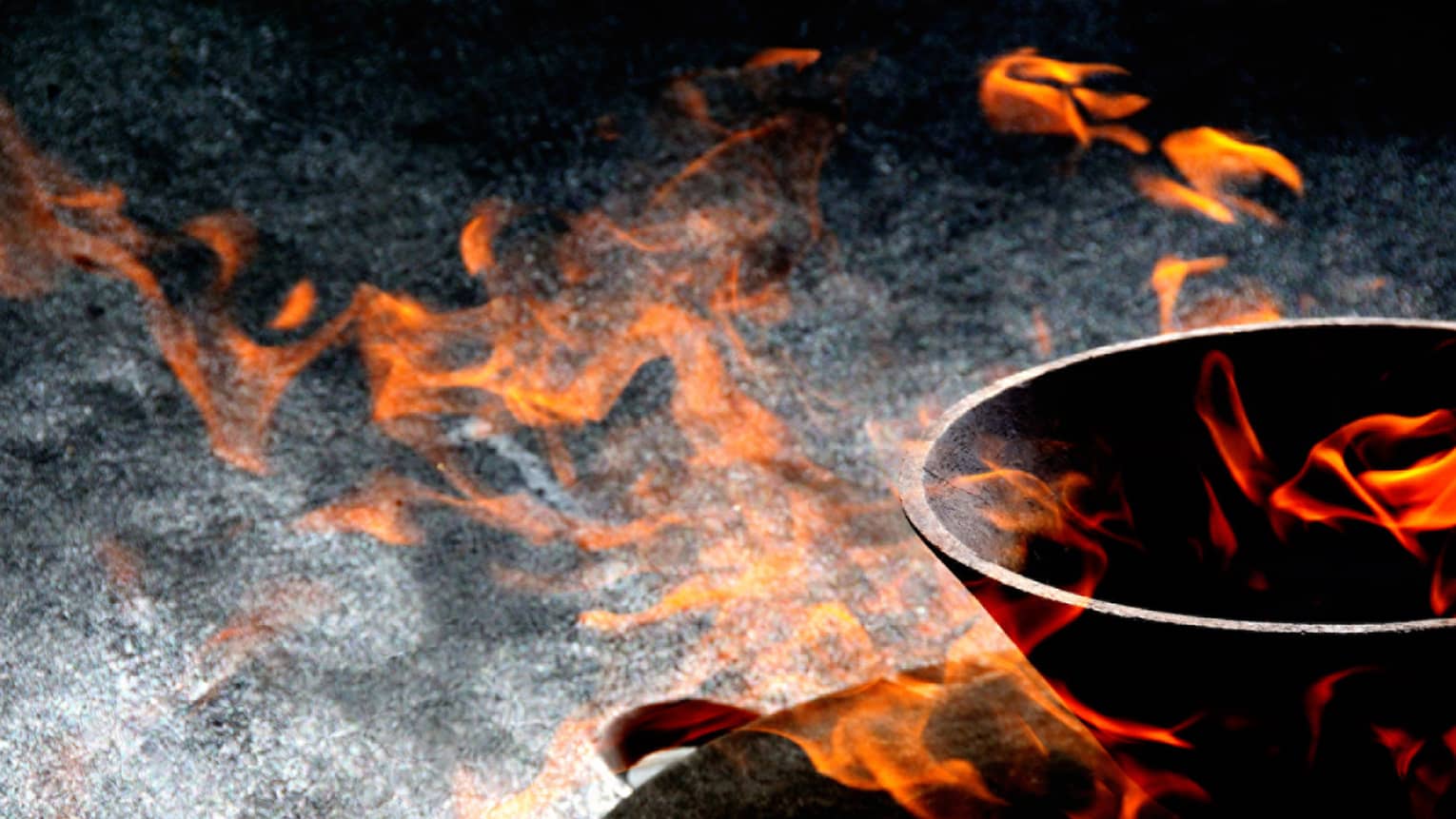 Close-up view of orange-red flames appearing to float in and around a stone bowl set against a variegated dark background.