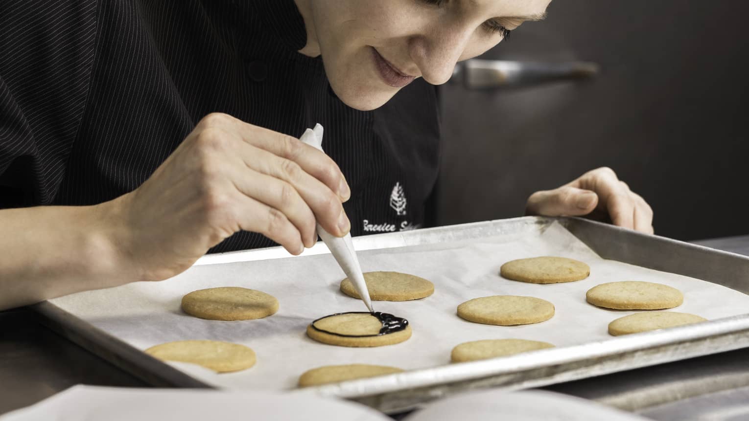 Pastry Chef adding chocolate garnish to row of cookies on baking pan