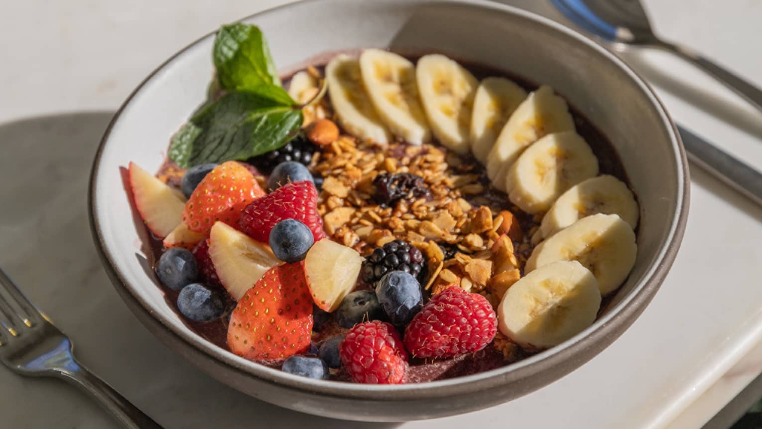 An a�a� bowl with strawberries, blueberries and bananas, and silverware on the side