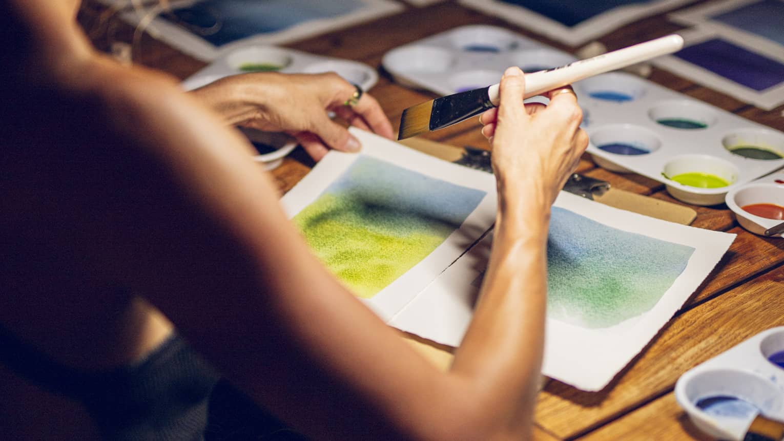 A woman painting a landscape on white paper with a brush