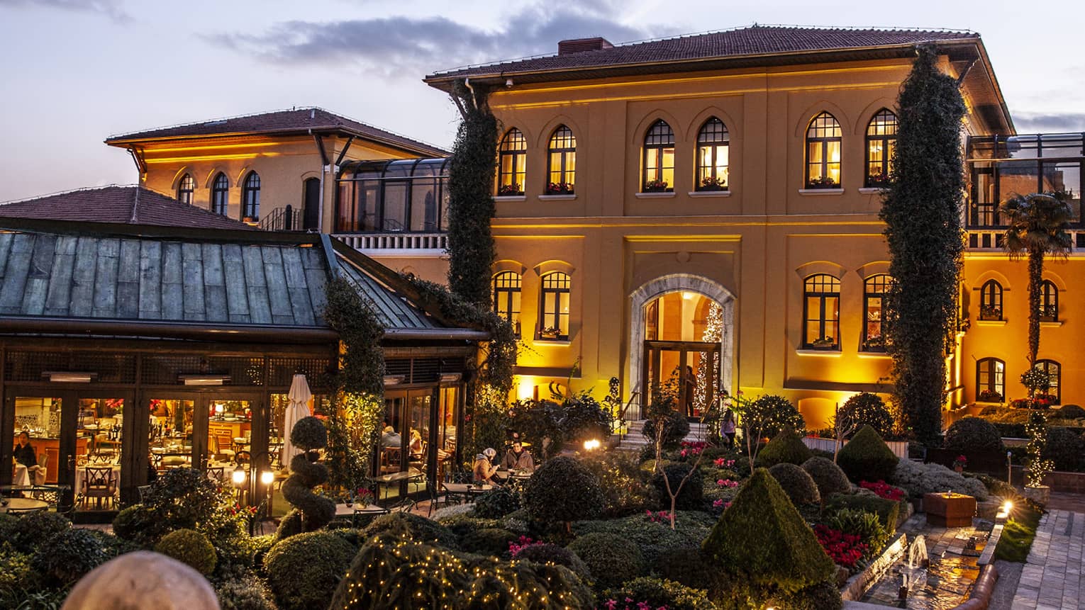 A courtyard at dusk, with the warm glow of the lights on in Hotel in the background