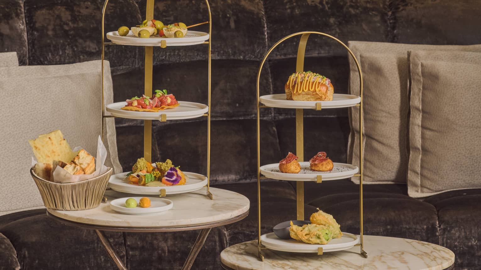 Three-tiered serving stands hold small bites and sit on small round tables in a restaurant setting.