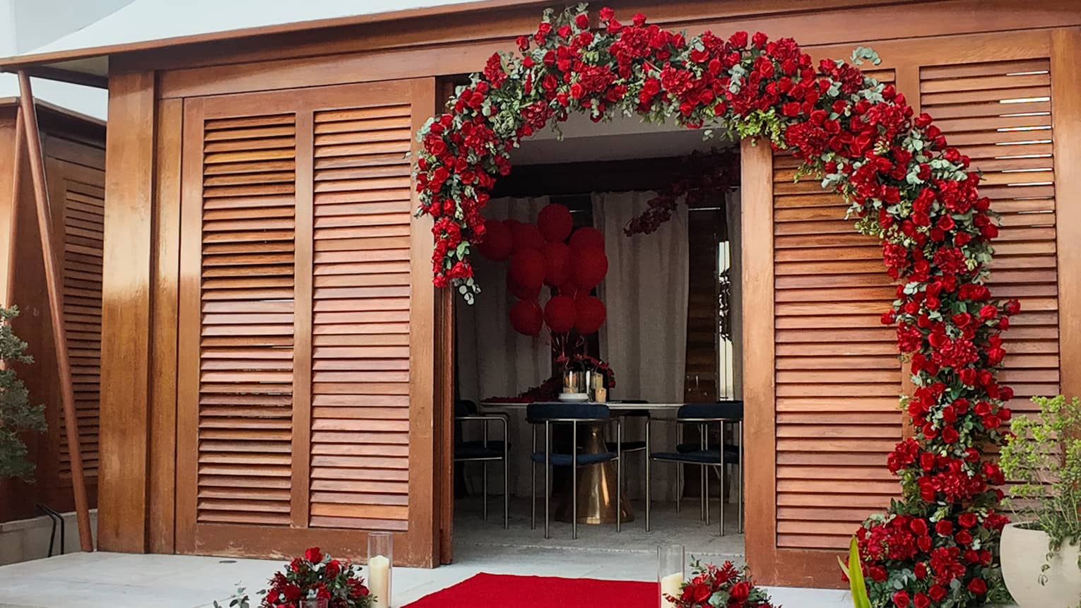 Poolside cabana entrance decorated with a red carpet lined with candles and a floral arch made of red roses