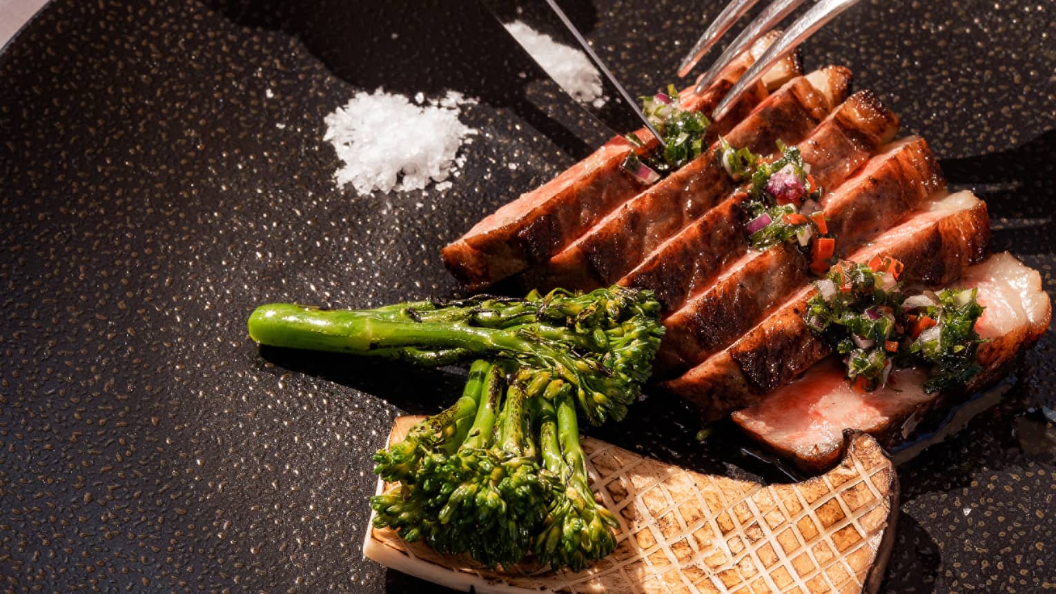 A cut of Wagyu beef tossed with salt and steamed broccoli on a black plate.