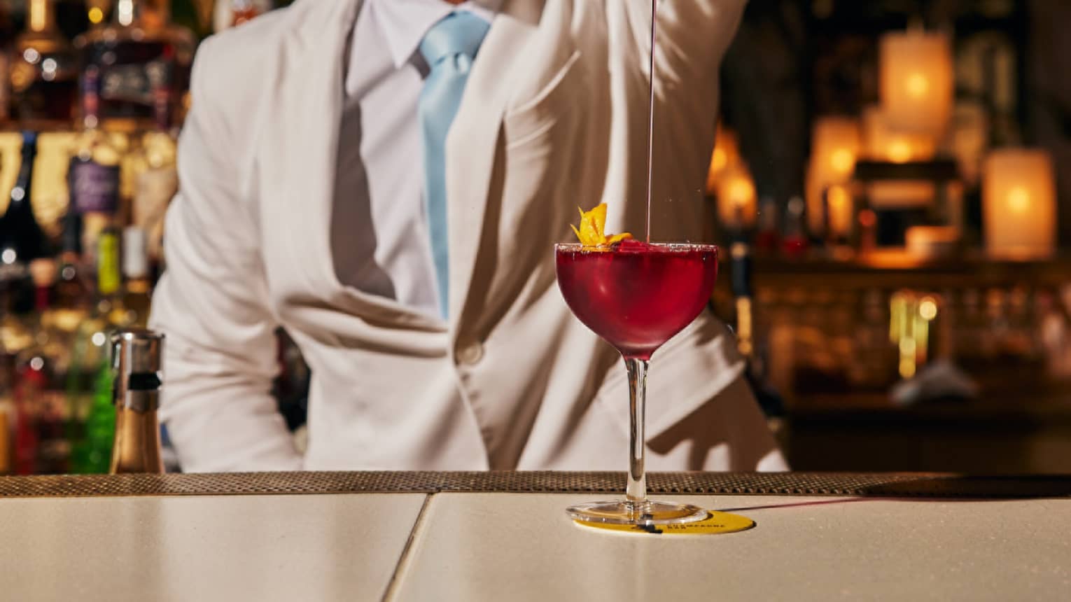 Bartender pours a cocktail from a silver cocktail shaker into a glass