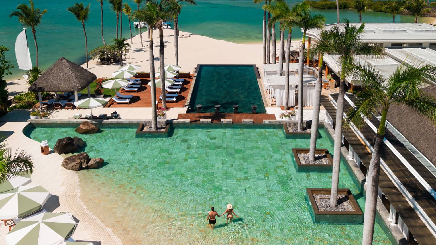 Aerial view of a resort pool adjacent to white-sand tropical beach