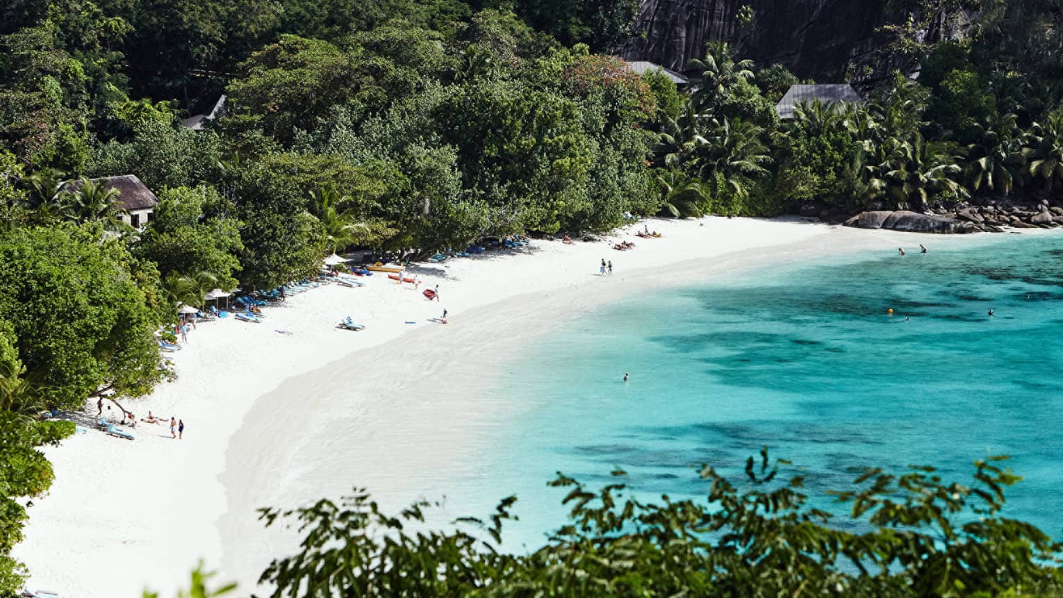 Aerial view of people on white sand beach surrounded by ocean and lush greenery 