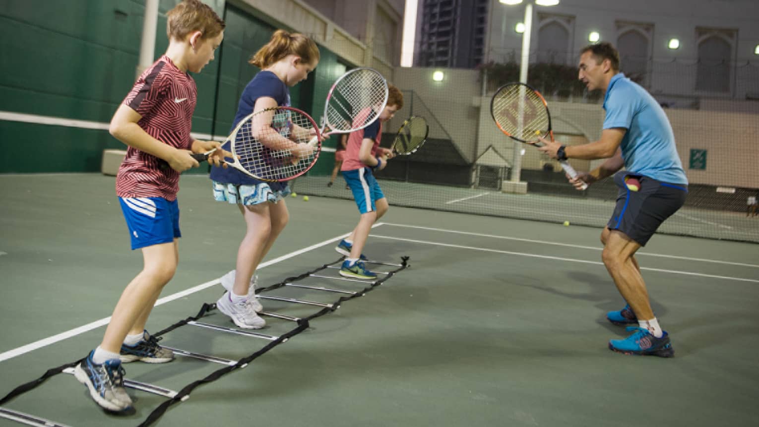 Tennis lesson, three children hold rackets, practice on tennis court in front of coach