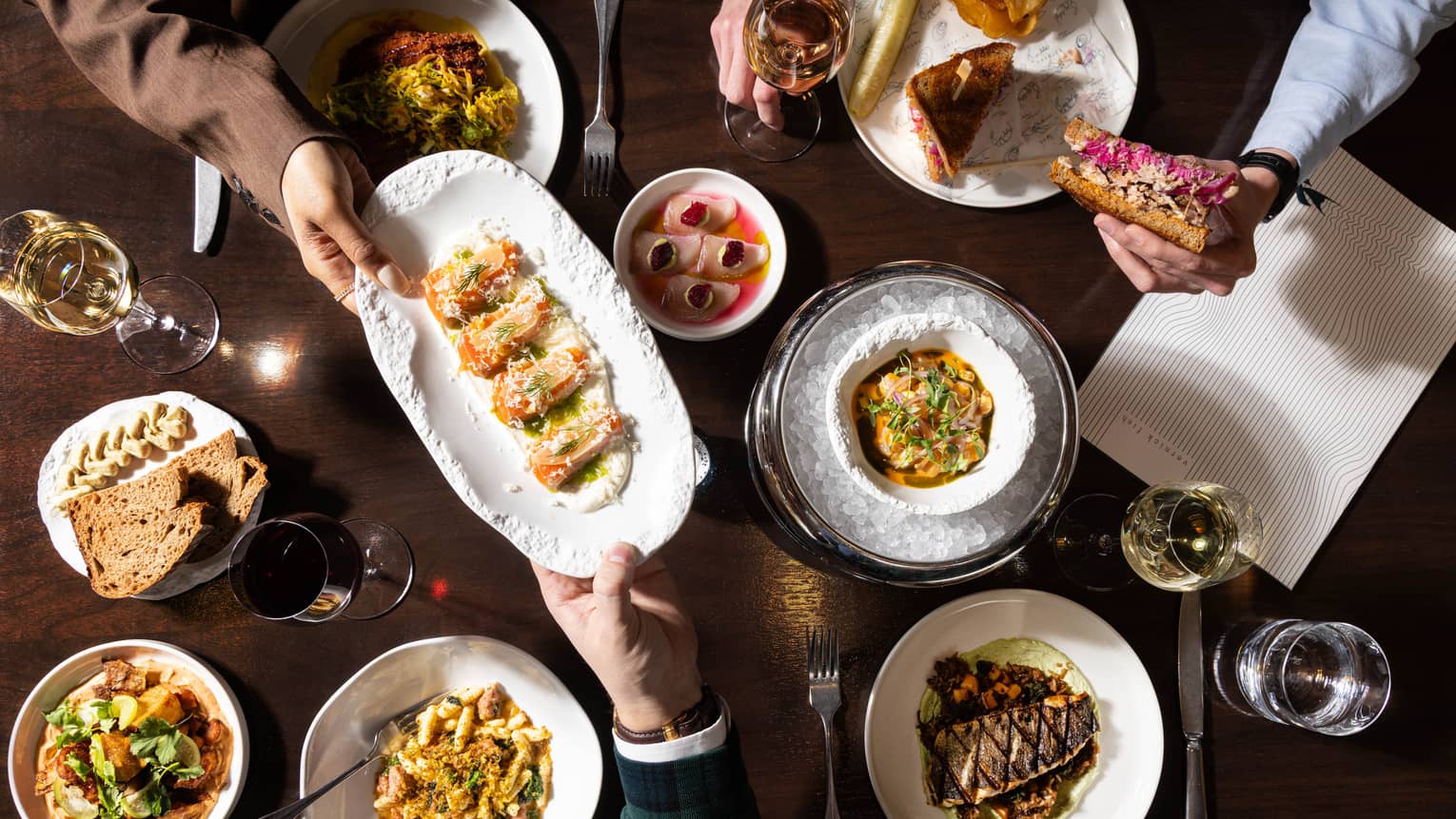 A dark wooden table topped with various colourful culinary dishes and glasses of wine