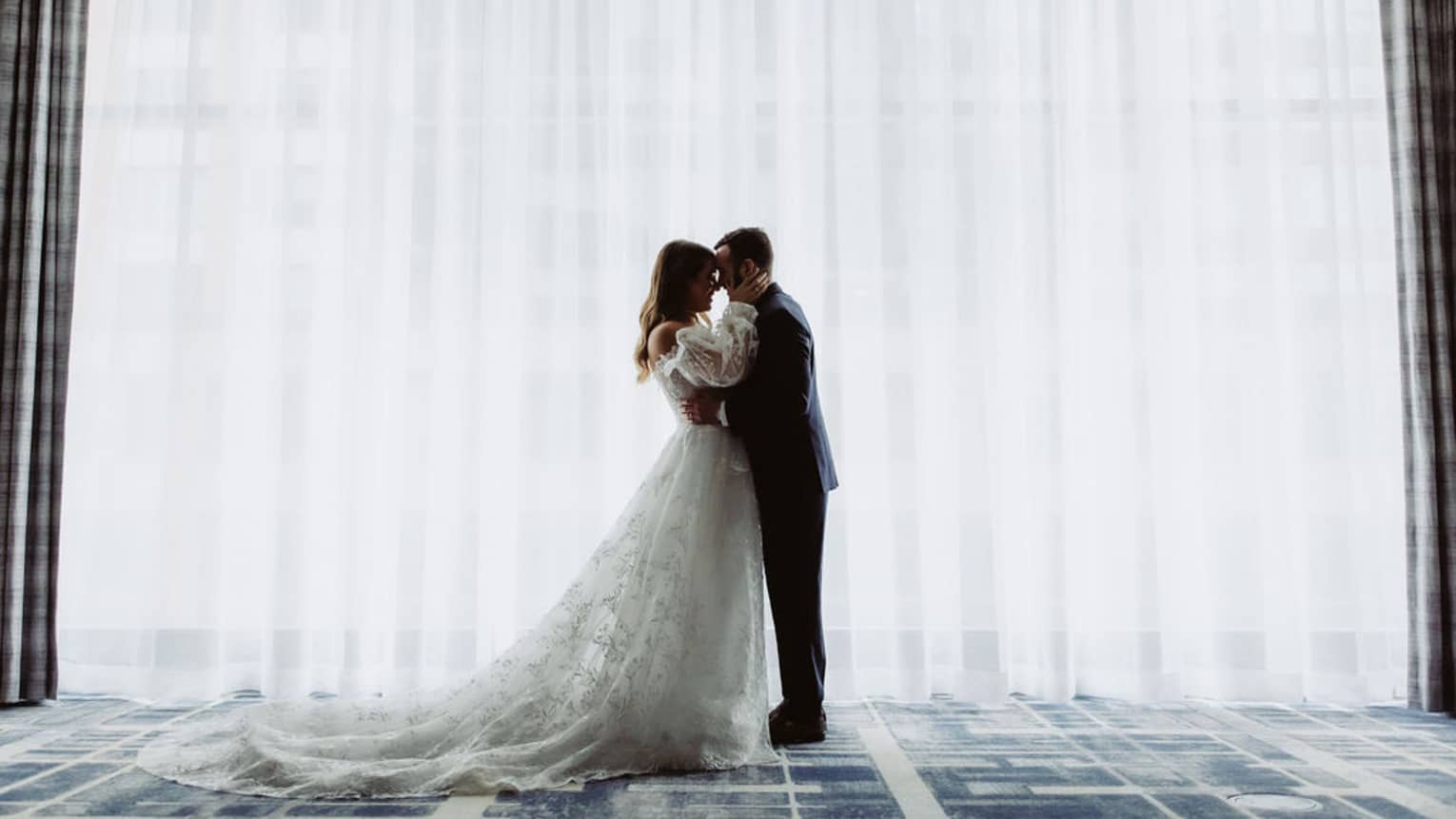 A woman and man in a wedding dress and suit standing in front of a curtain.