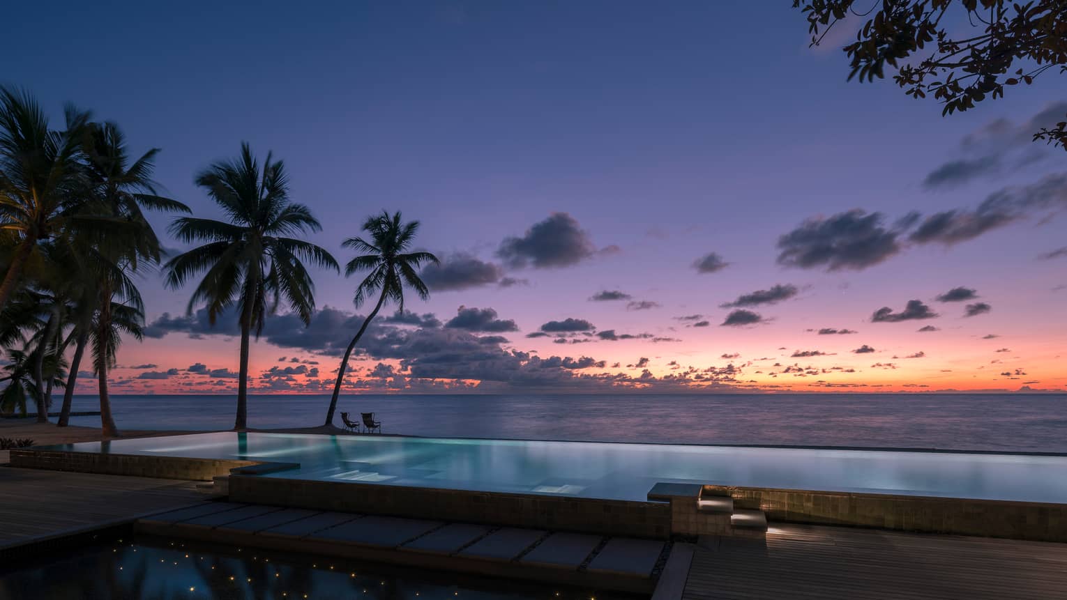 Beach pool with palm trees and water views at sunset