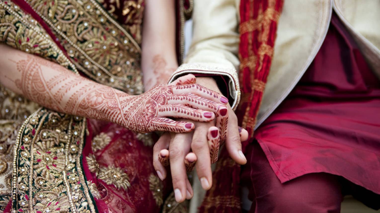 Indian wedding ceremony, bride with henna designs on arm holds groom's hands