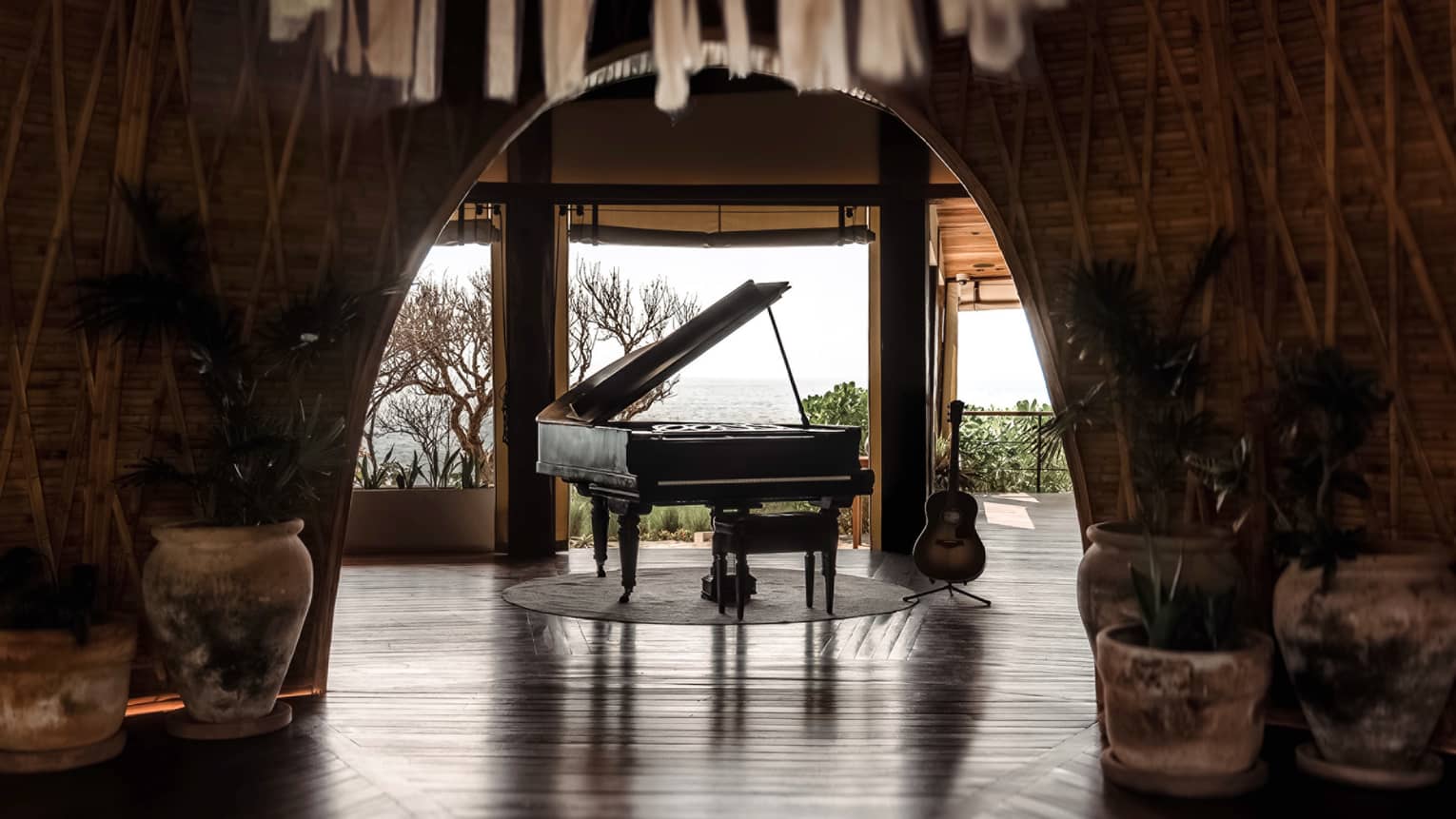 Black grand piano sits in the centre of a room that opens up to the ocean in the distance