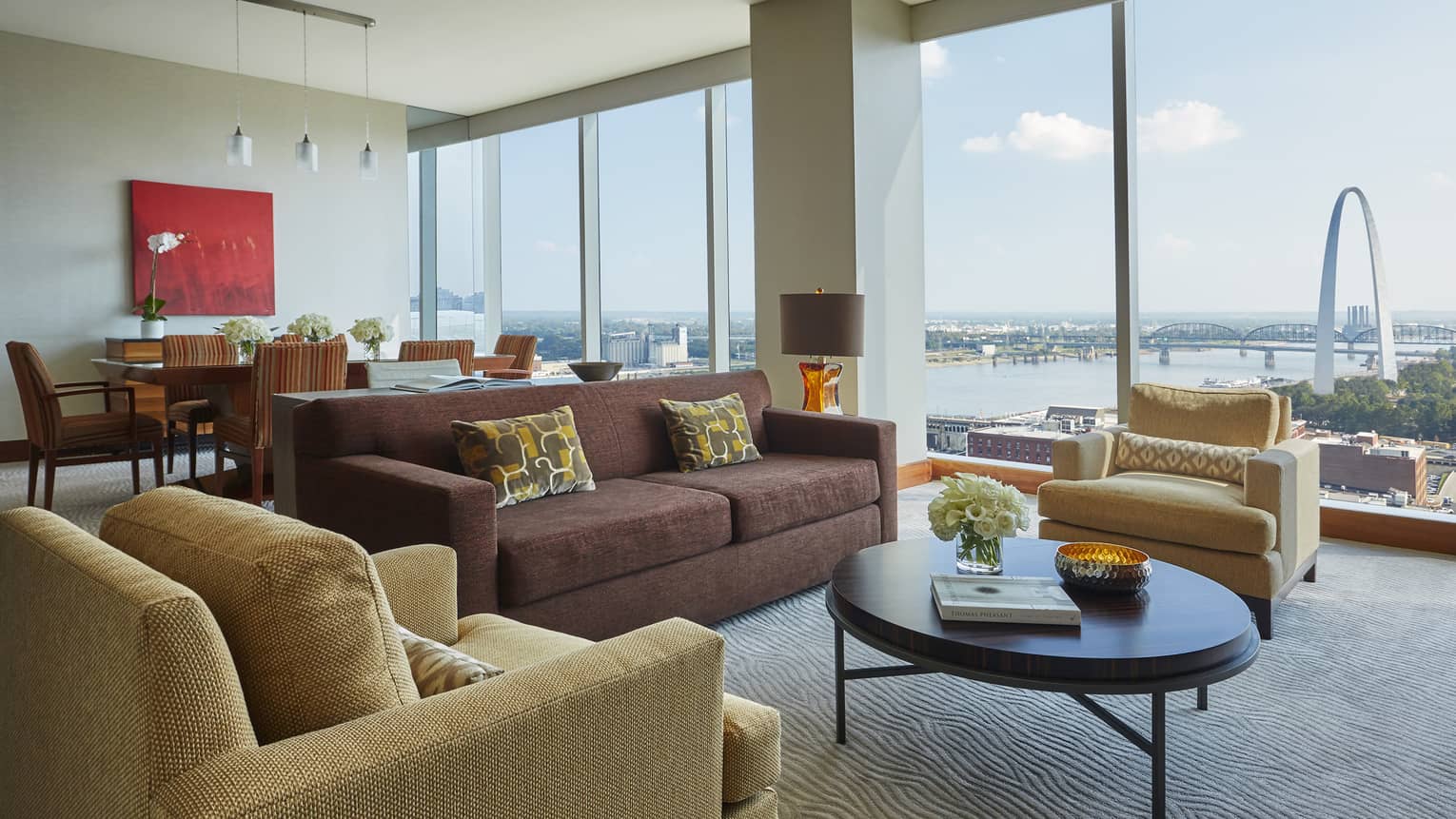 Luxury suite living room with burgundy sofa, yellow armchairs, round coffee table, tall windows with arch view