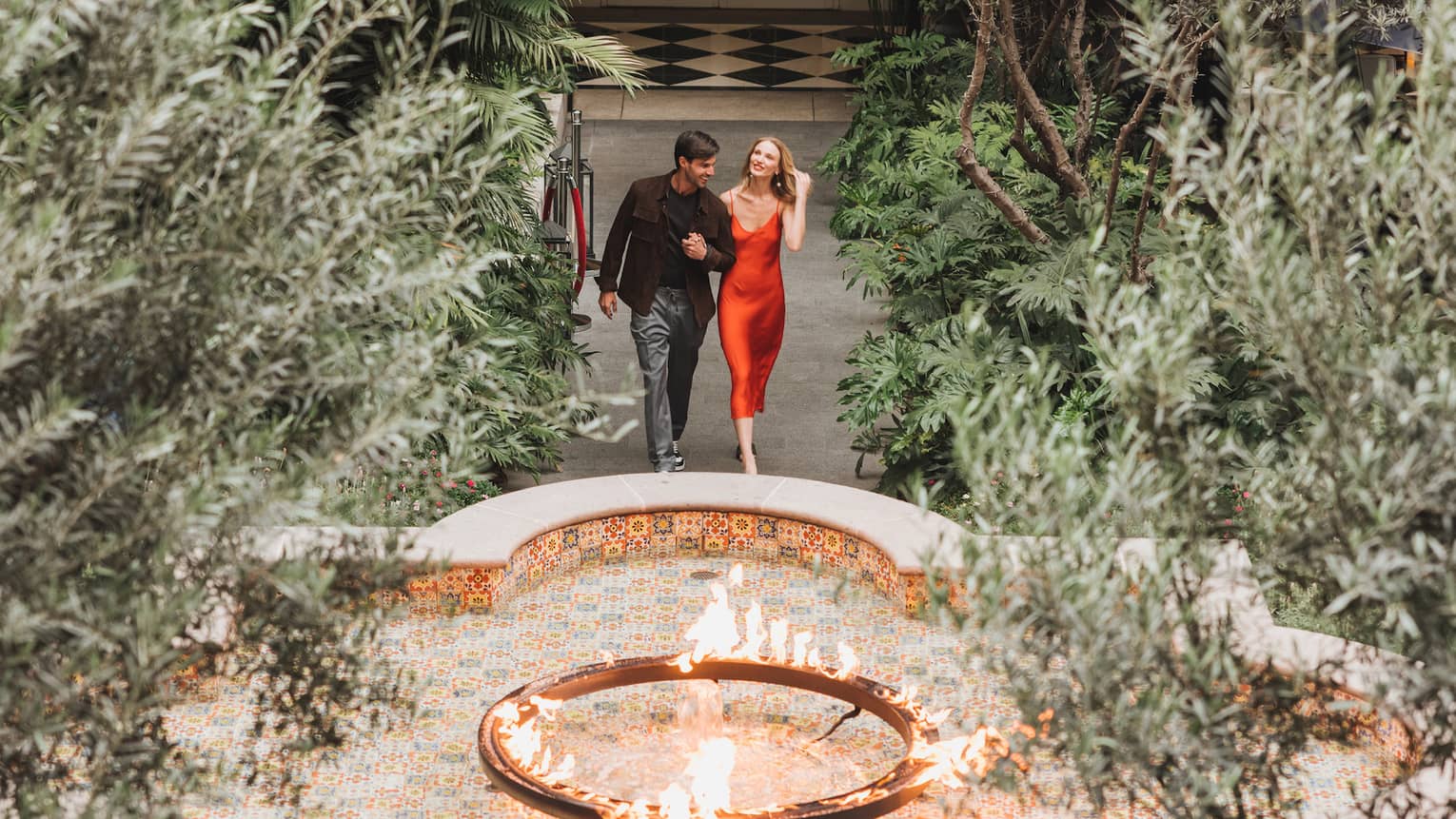A woman and man walking in a courtyard surrounded by plants and a small fountain.