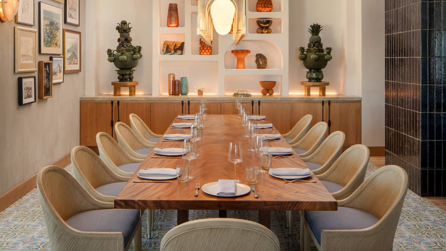 Rectangular dining table set for 11 in a private dining room with blue-tile flooring and a white accent wall with arched shelving