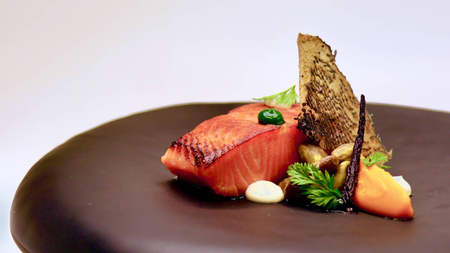 Salmon and garnishes on a black plate.
