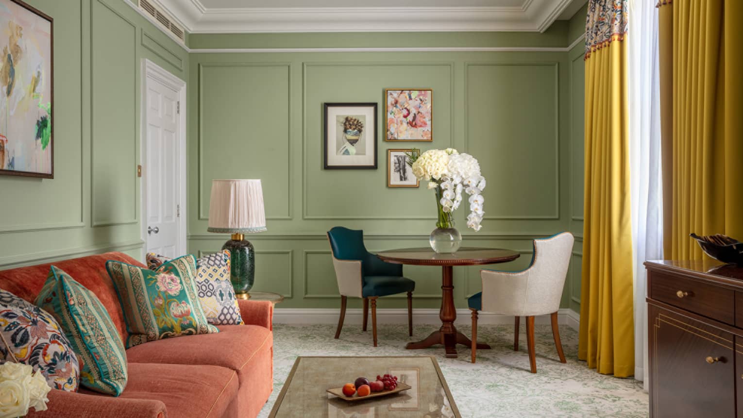 Guest room with red couch, coffee table, small round table with two leather chairs, avocado-coloured walls, window with yellow drapes