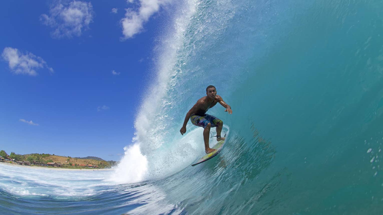 A man surfing through a wave during a bright and sunny day.