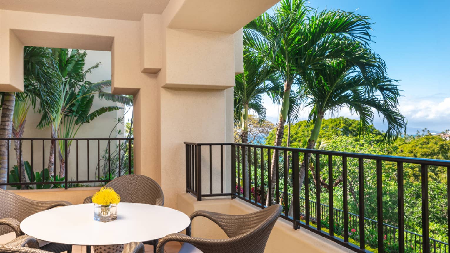 Luxury resort balcony with round table, yellow flowers, wicker chairs and view of tropical palm trees