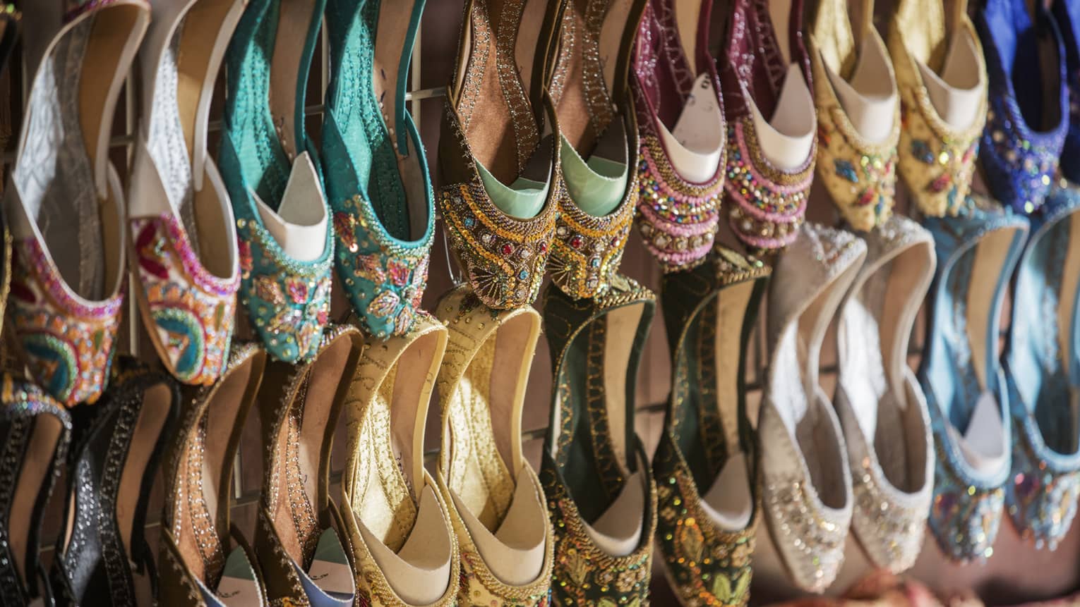 Rows of colourful shoes with beadwork and embroidery hang from market wall