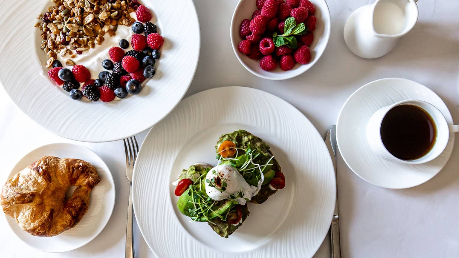 An assortment of food including avocado toast, yogurt, berries, and bread.