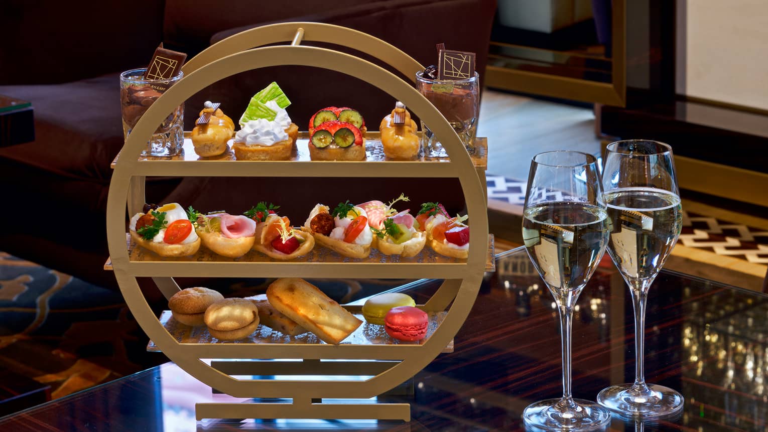 Afternoon tea three-tiered tray with selection of sandwiches and desserts, two glasses of white wine