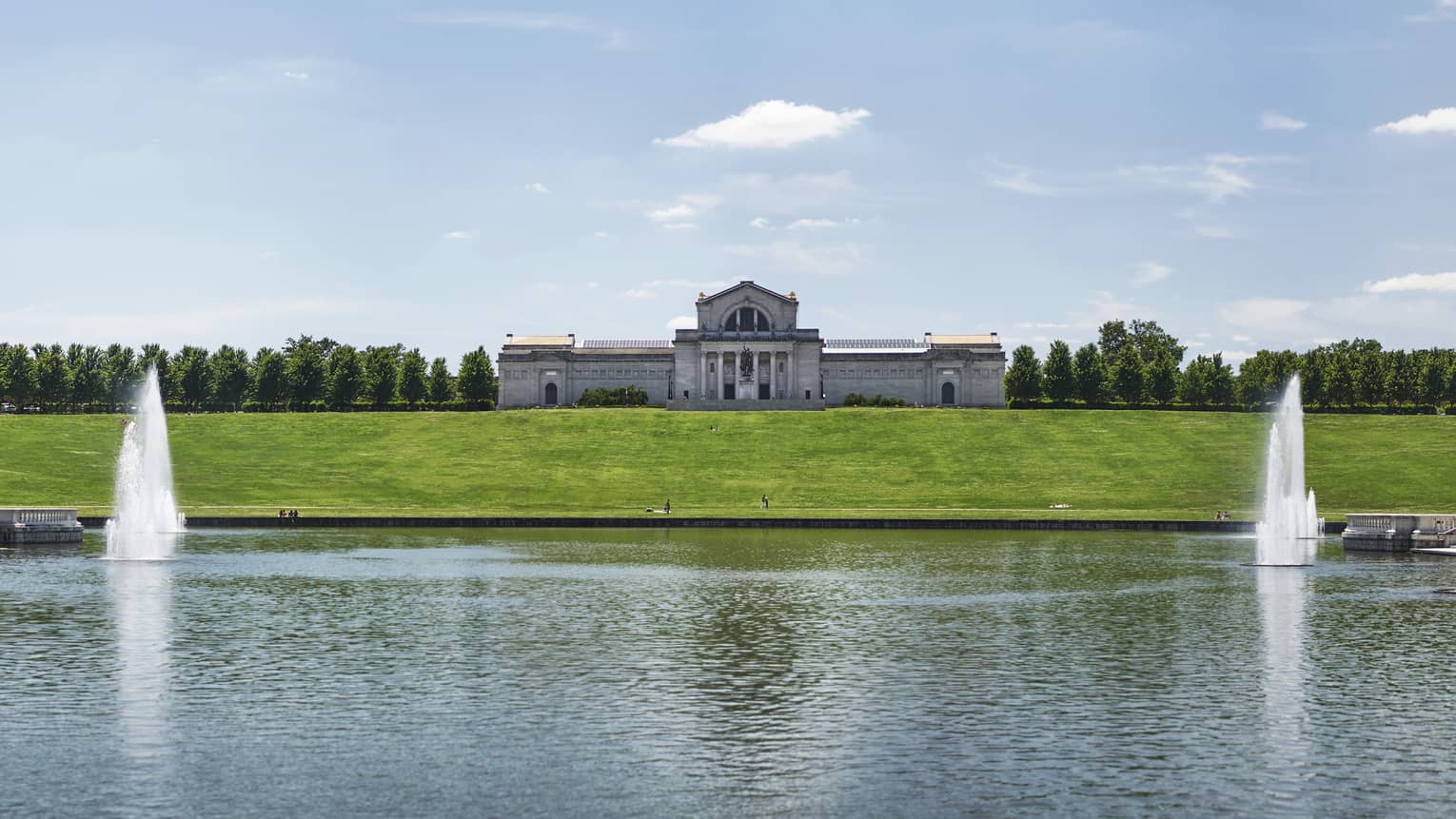 A large building with a lake in front of it with fountains.