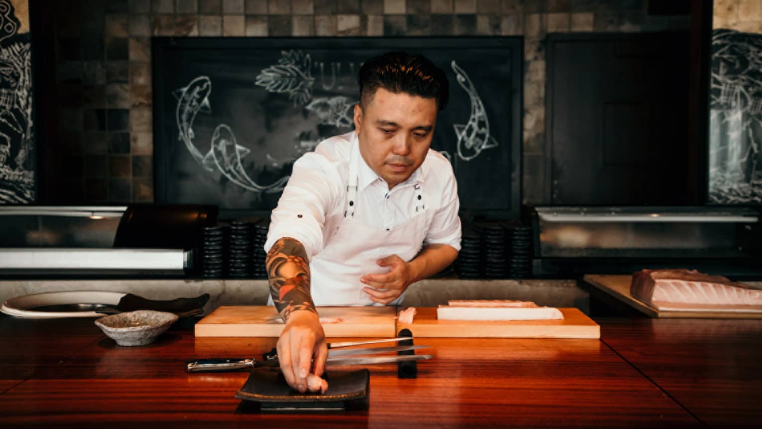 A male chef behind wooden counter places a piece of seafood on plate