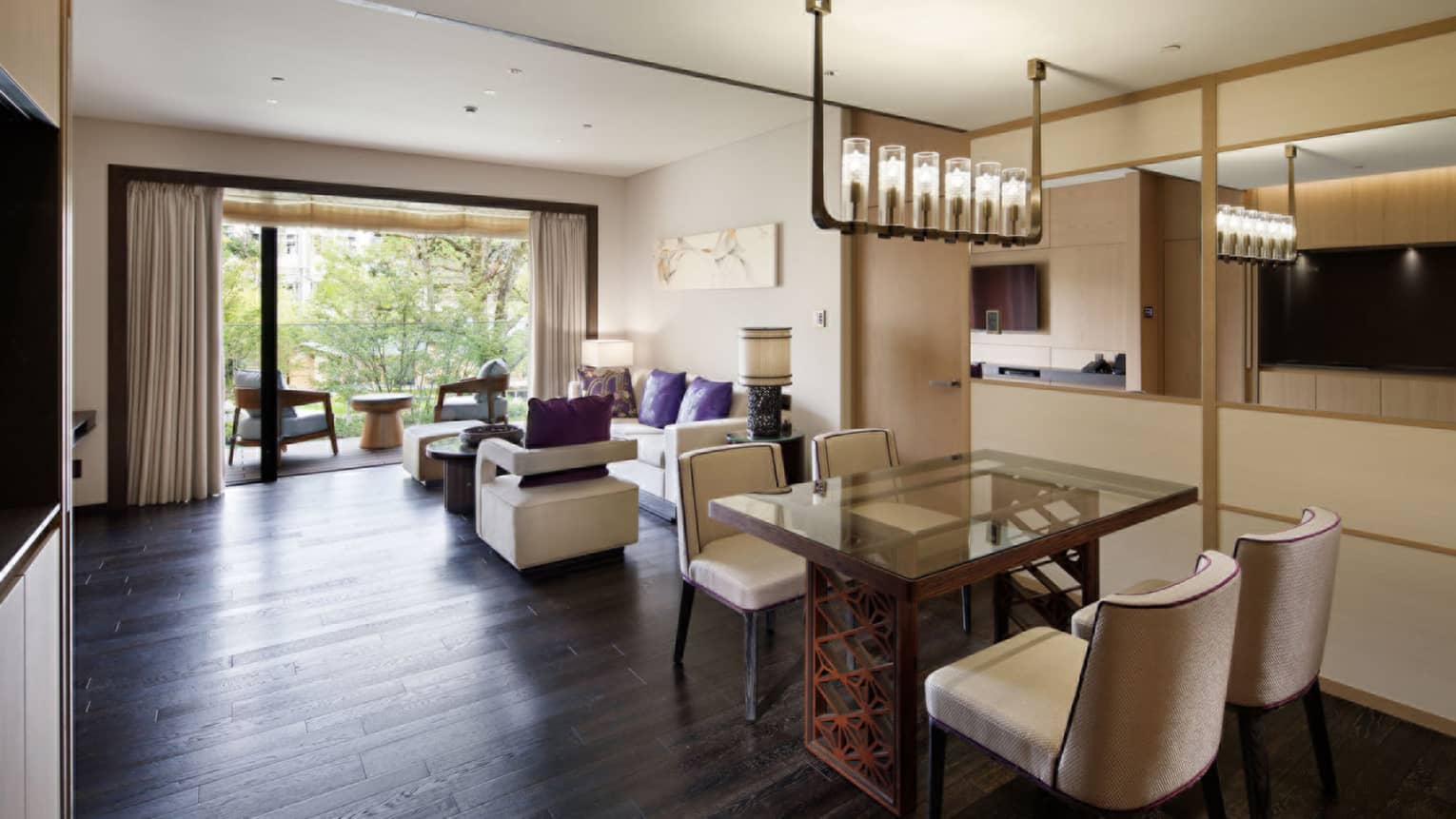 Spacious living and dining area with a glass dining table, chairs, a comfortable seating area and sliding doors opening to a balcony with garden view