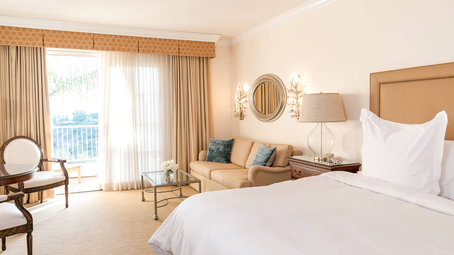 Hotel villa bedroom, bed and seating area by sunny floor-to-ceiling patio door 