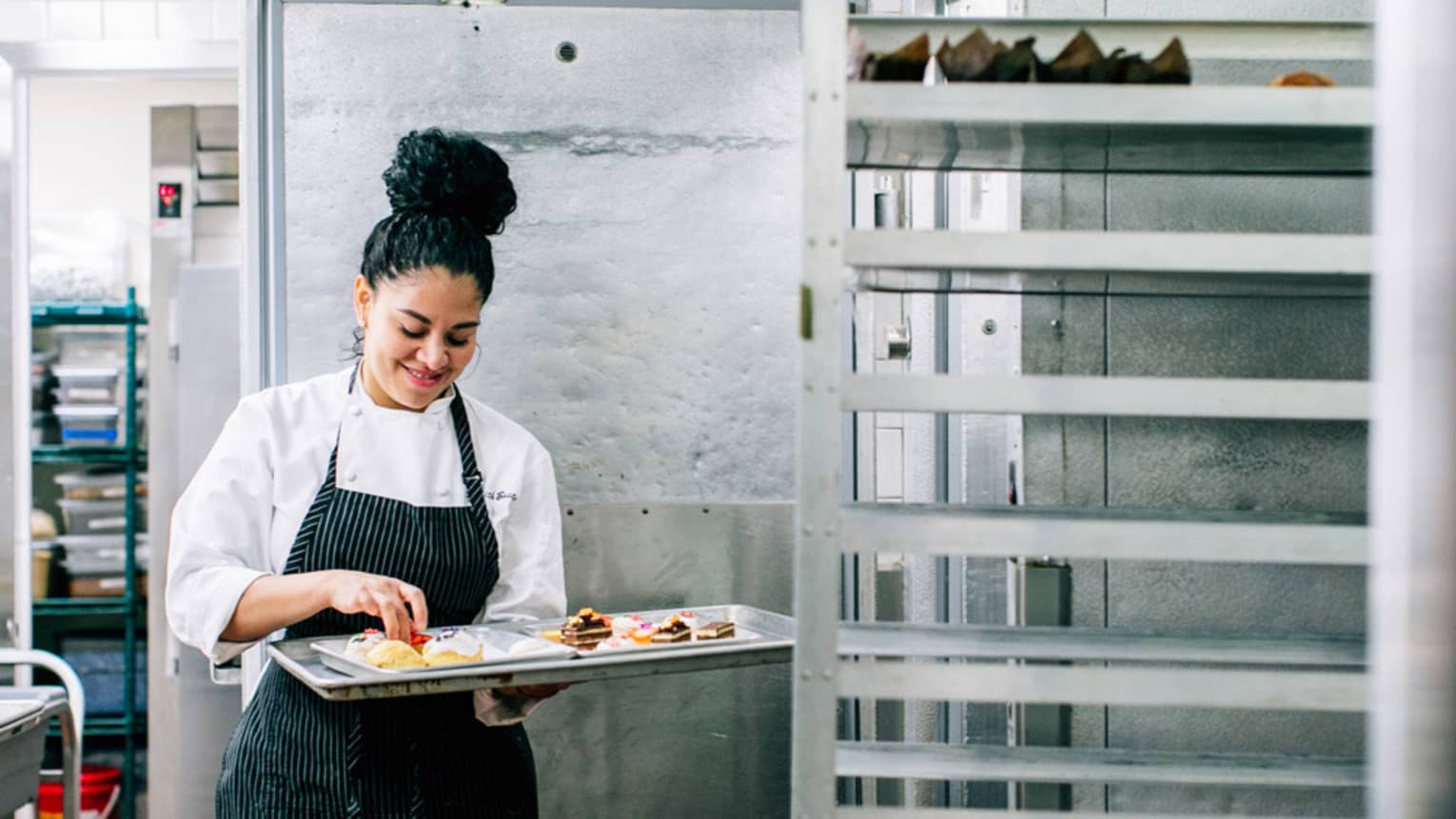 A chef in an apron prepares pastries from a baking rack in the kitchen