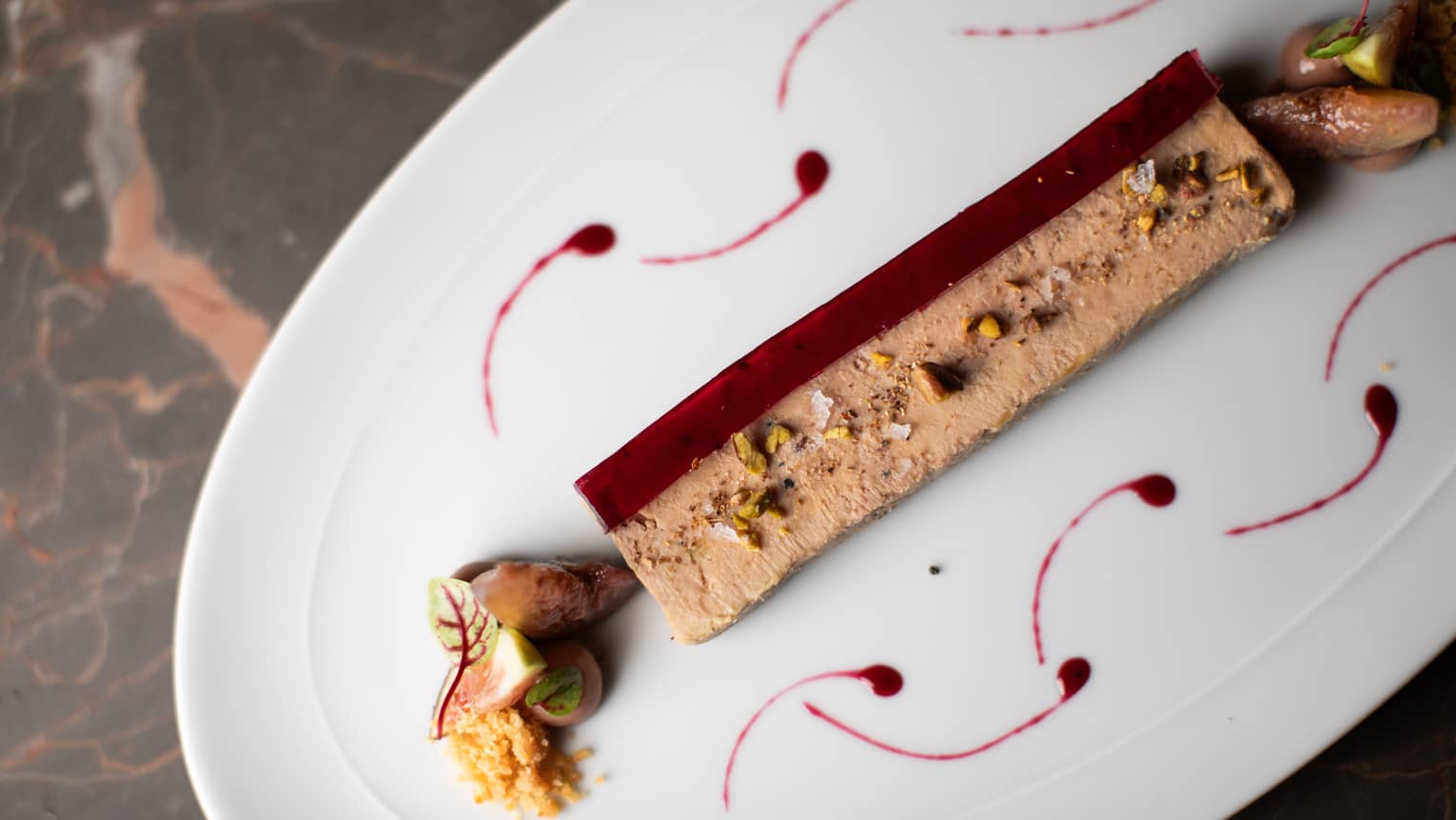 Rectangular foie gras with nuts and garnishes on either side plated on a white oval dish
