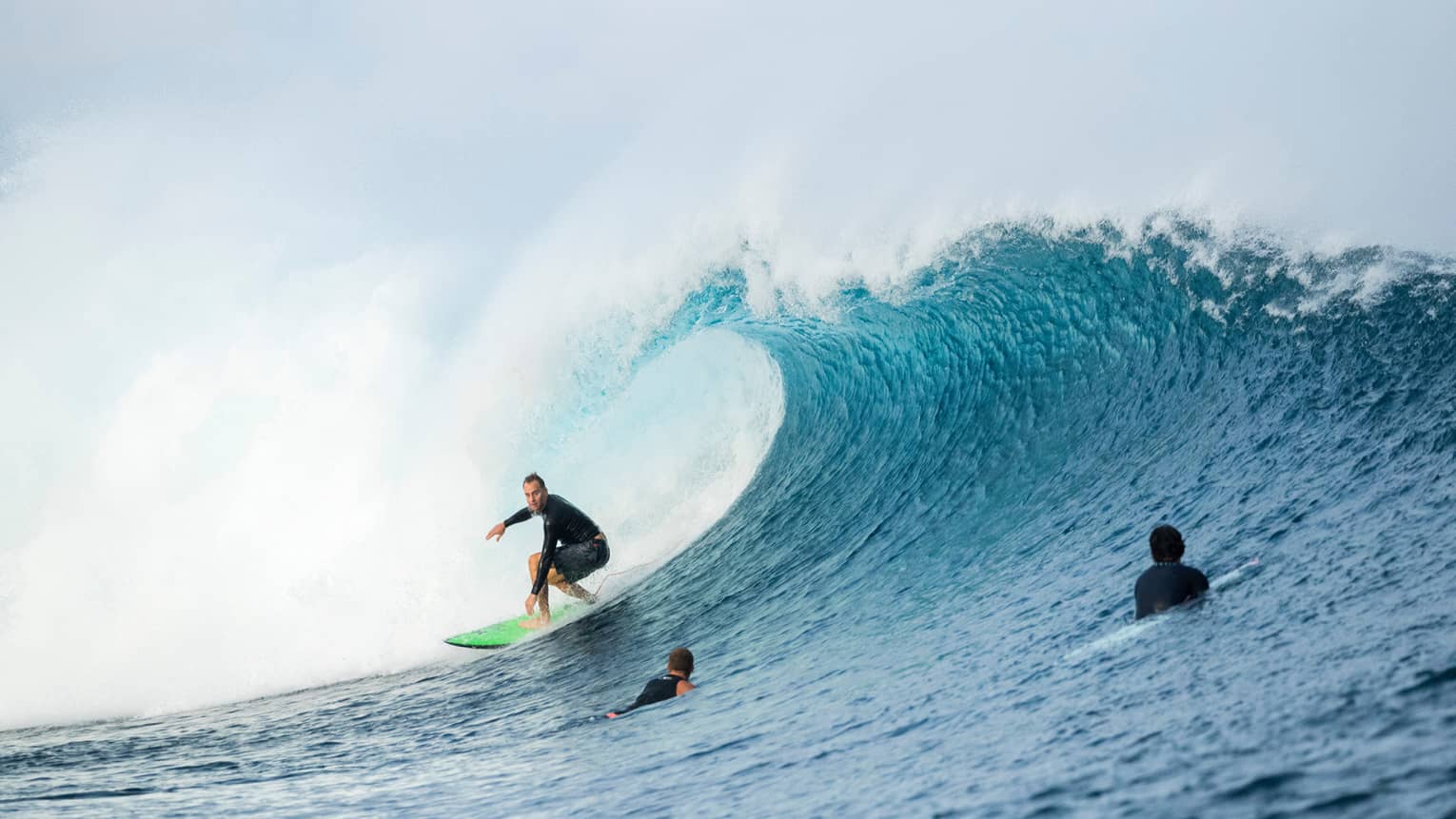 Surfer rides surfboard on large wave, two surfers swimming in water