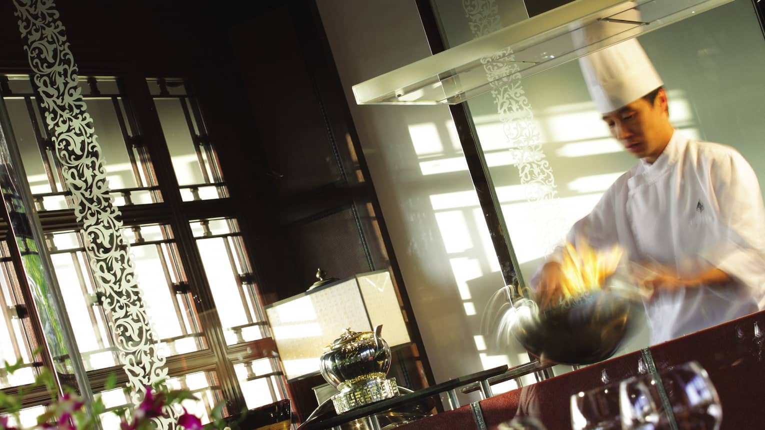 Chef in white uniform tosses food in silver bowl in Jin Sha kitchen