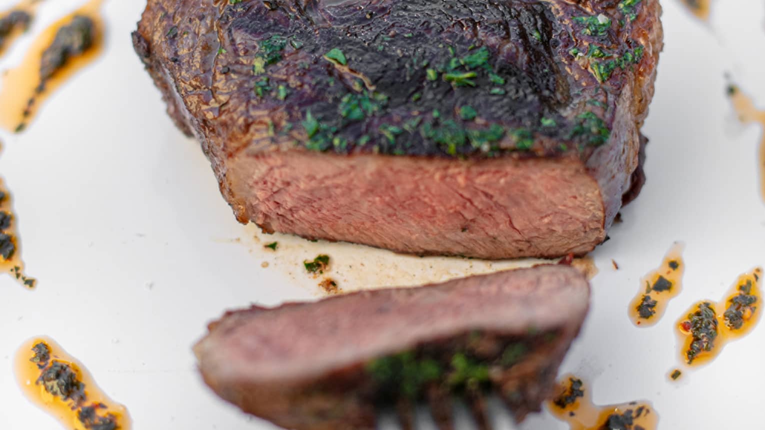 A fork pulling a piece of sirloin across a plate.