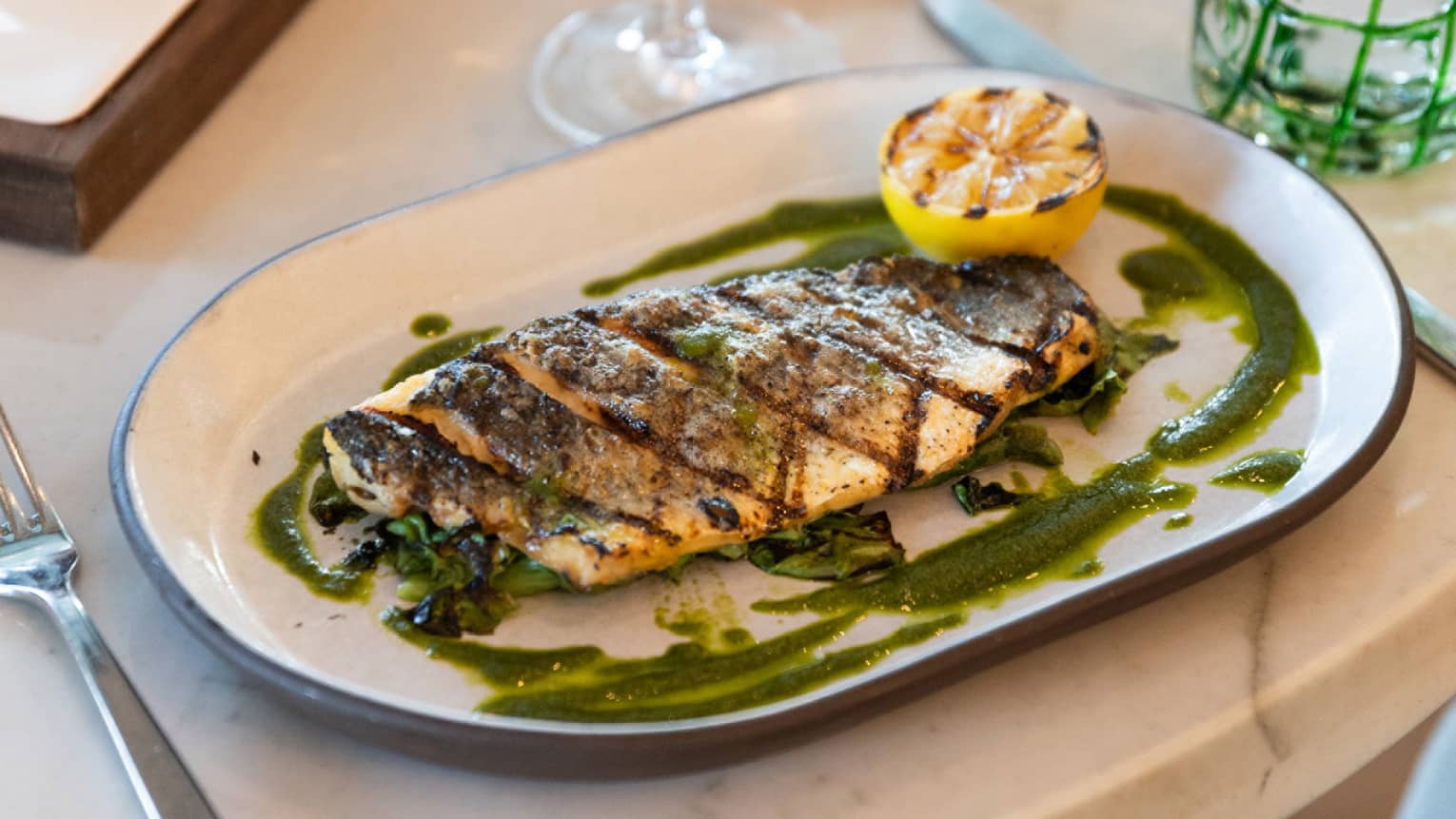 A plate of branzino with silverware on the side and a wine glass