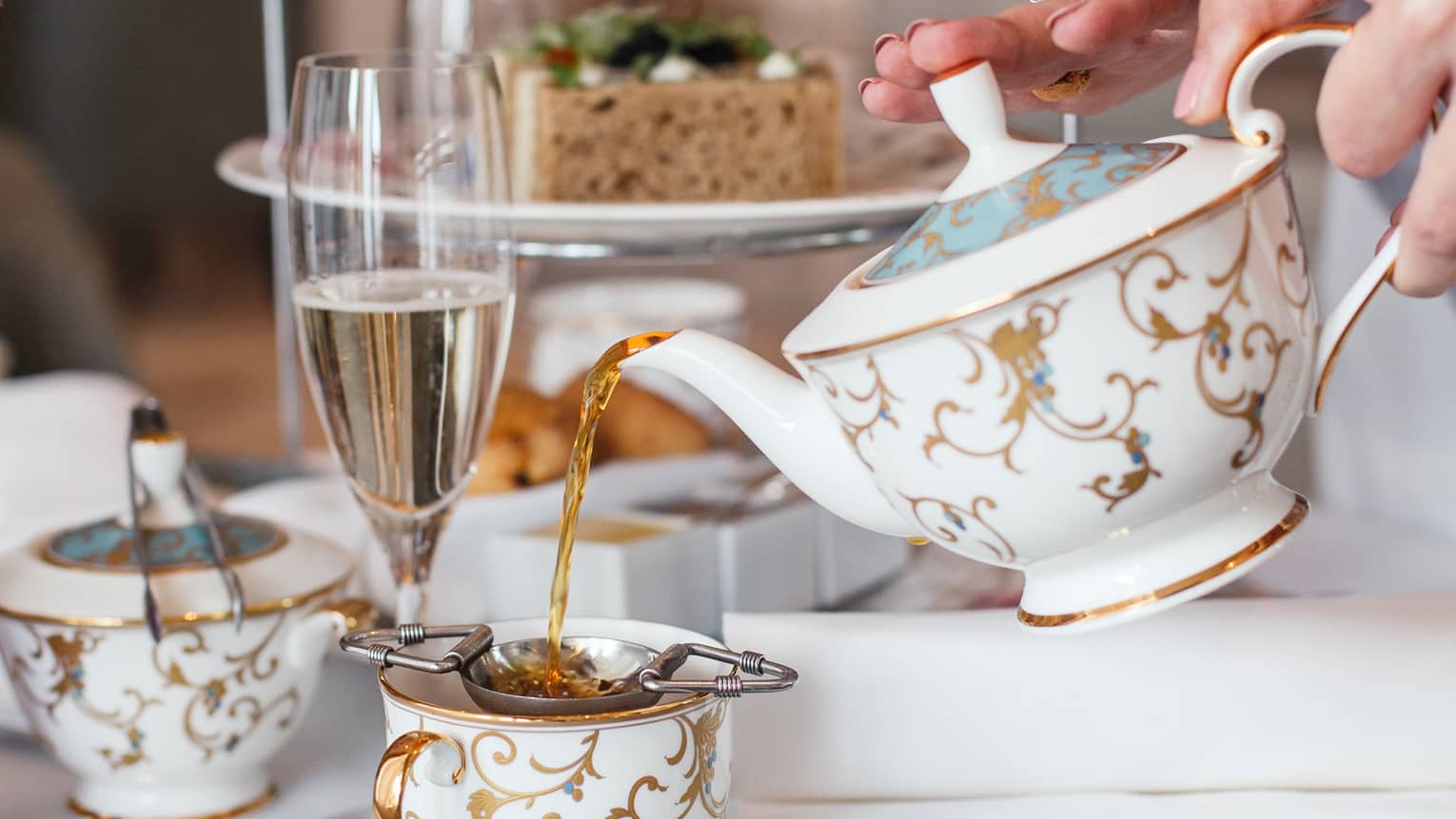 Hotel staff pours gold and white teapot by dessert tray at afternoon tea 