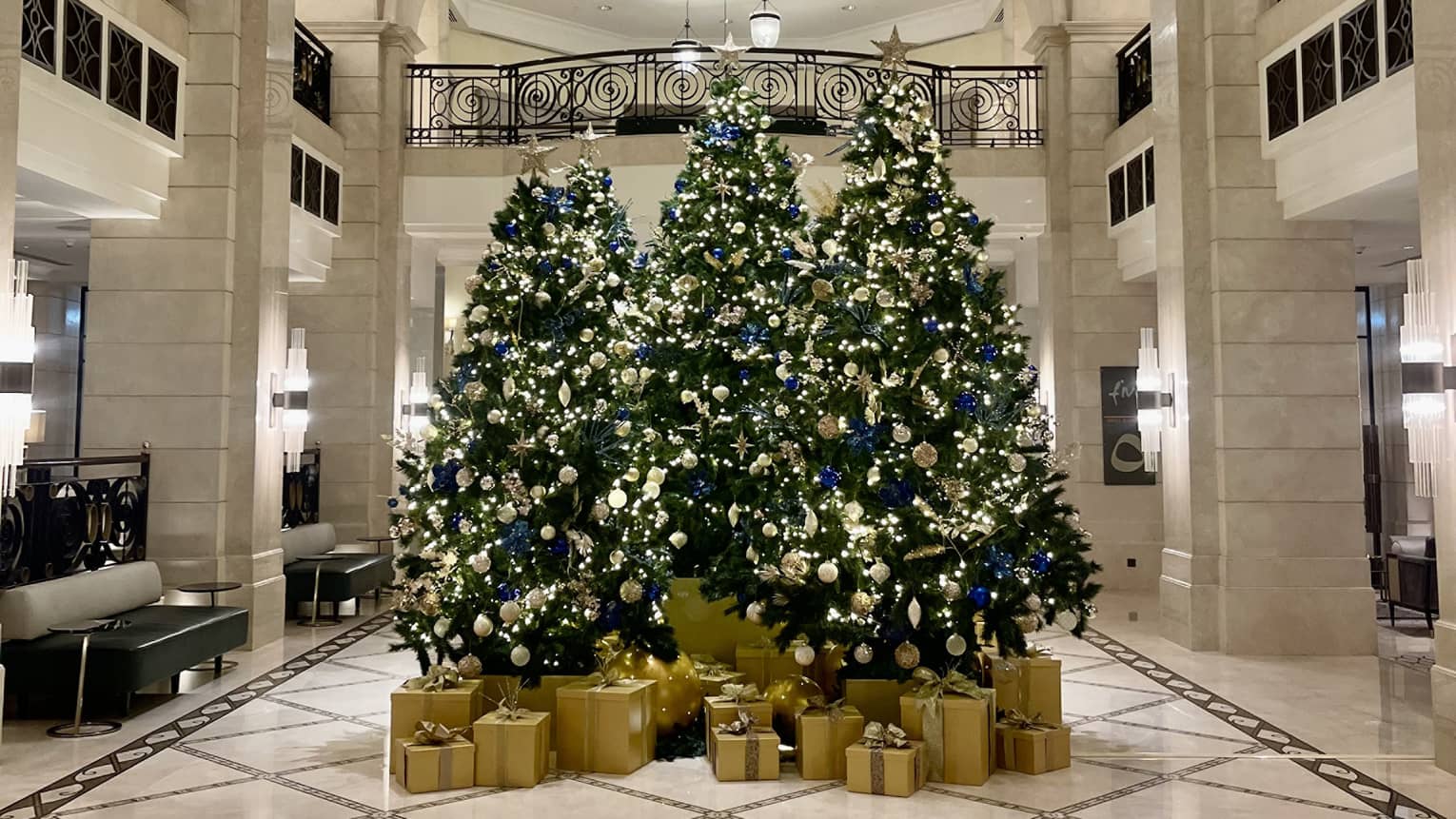 Three Christmas trees decorated in gold sit in the center of the Hotel lobby, with gold-wrapped boxes of presents beneath each one