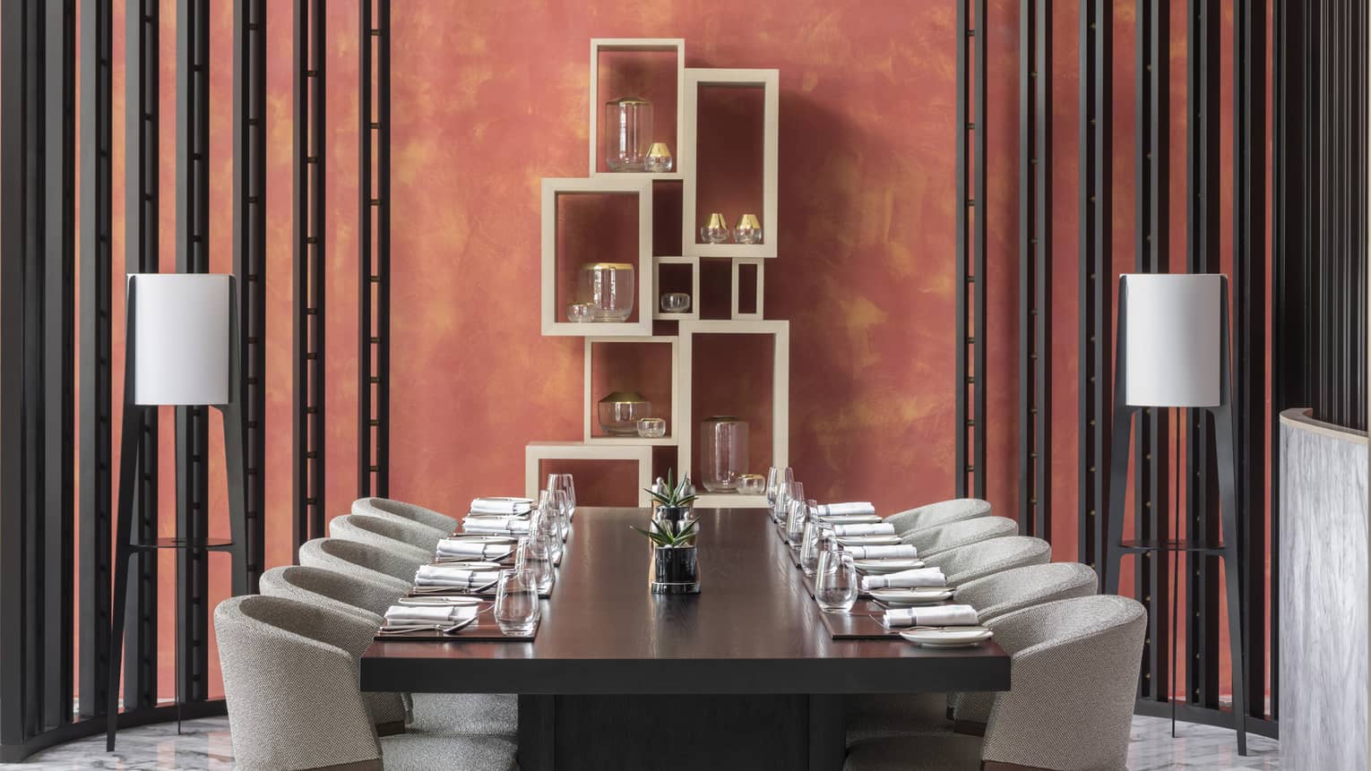 A sculptural lighting fixture hangs above a set table in a coral dining room