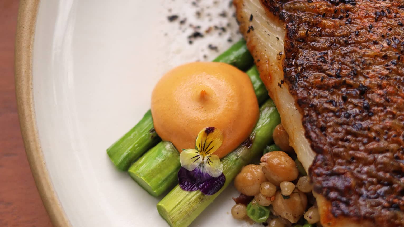 Grilled red snapper seasoned with Moroccan spices, served over aromatic couscous with sweet peas and asparagus, accompanied by tahini.