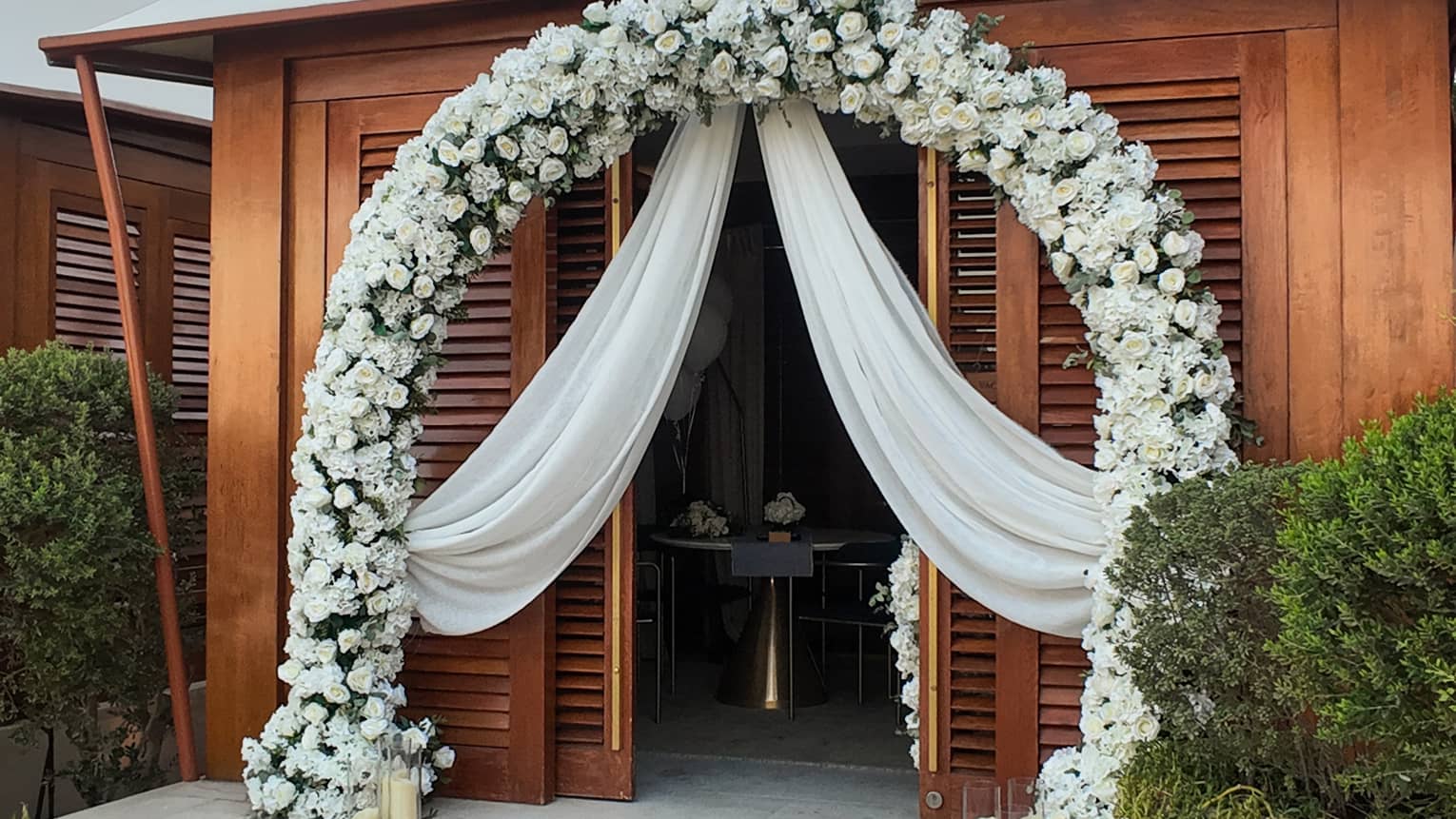 Poolside cabana decorated with a red carpet on the stairs and a large white floral arch way and curtains draping over the entrance