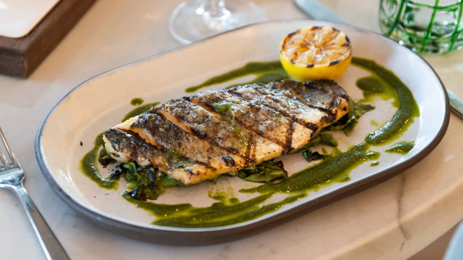 A plate of branzino with silverware on the side and a wine glass