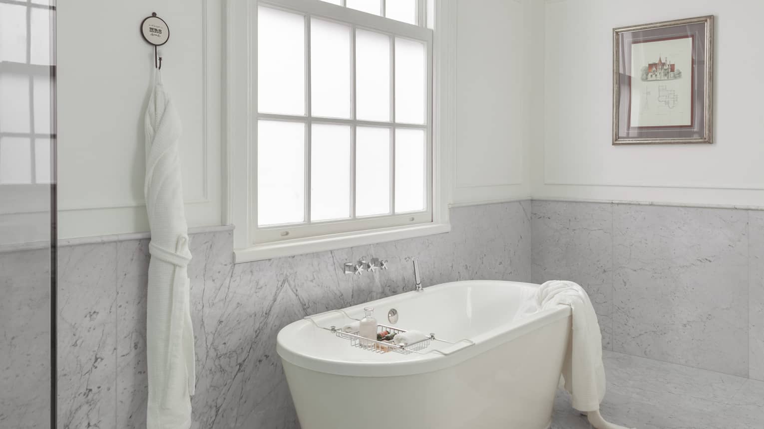 Elegant luxury hotel bathroom with standalone deep soaking tub next to a window, and marble floors