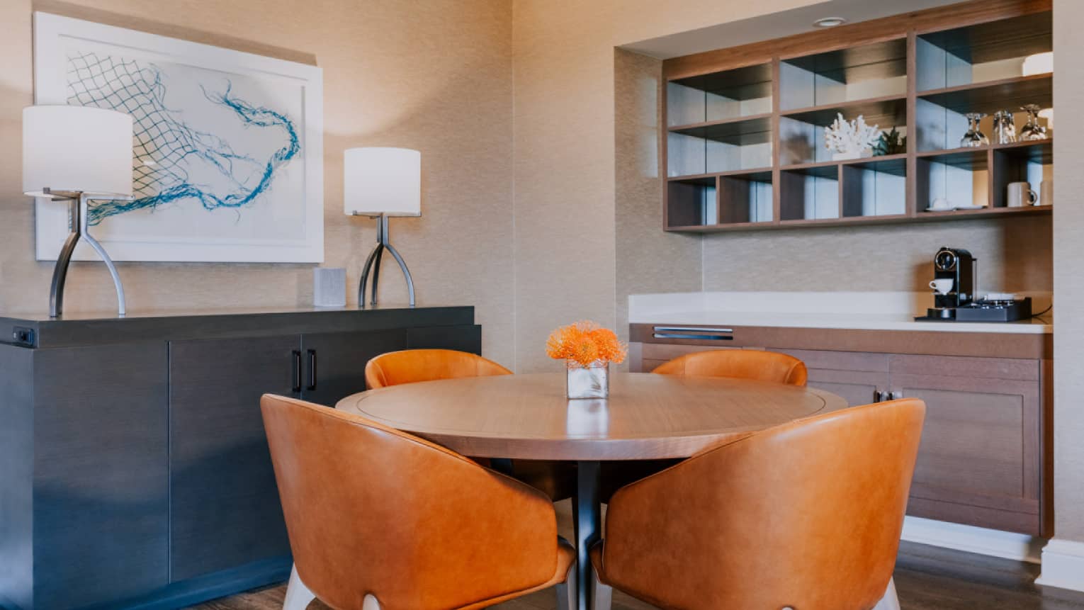 Dining nook with round table, four orange chairs, built-in shelves and coffee station with wall art and lamps