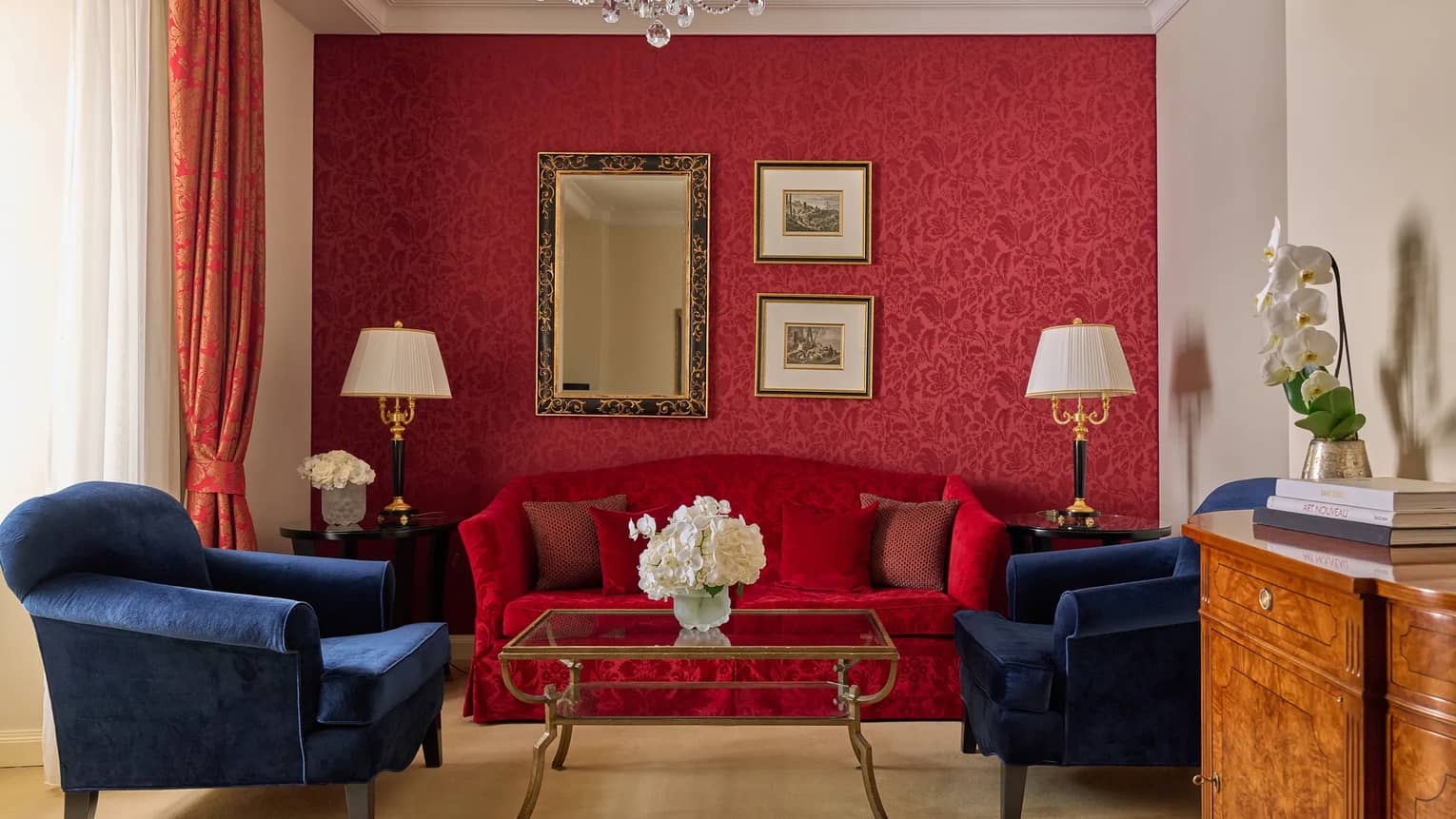 Elegant hotel room featuring red accent wall, red love seat and two dark blue arm chairs