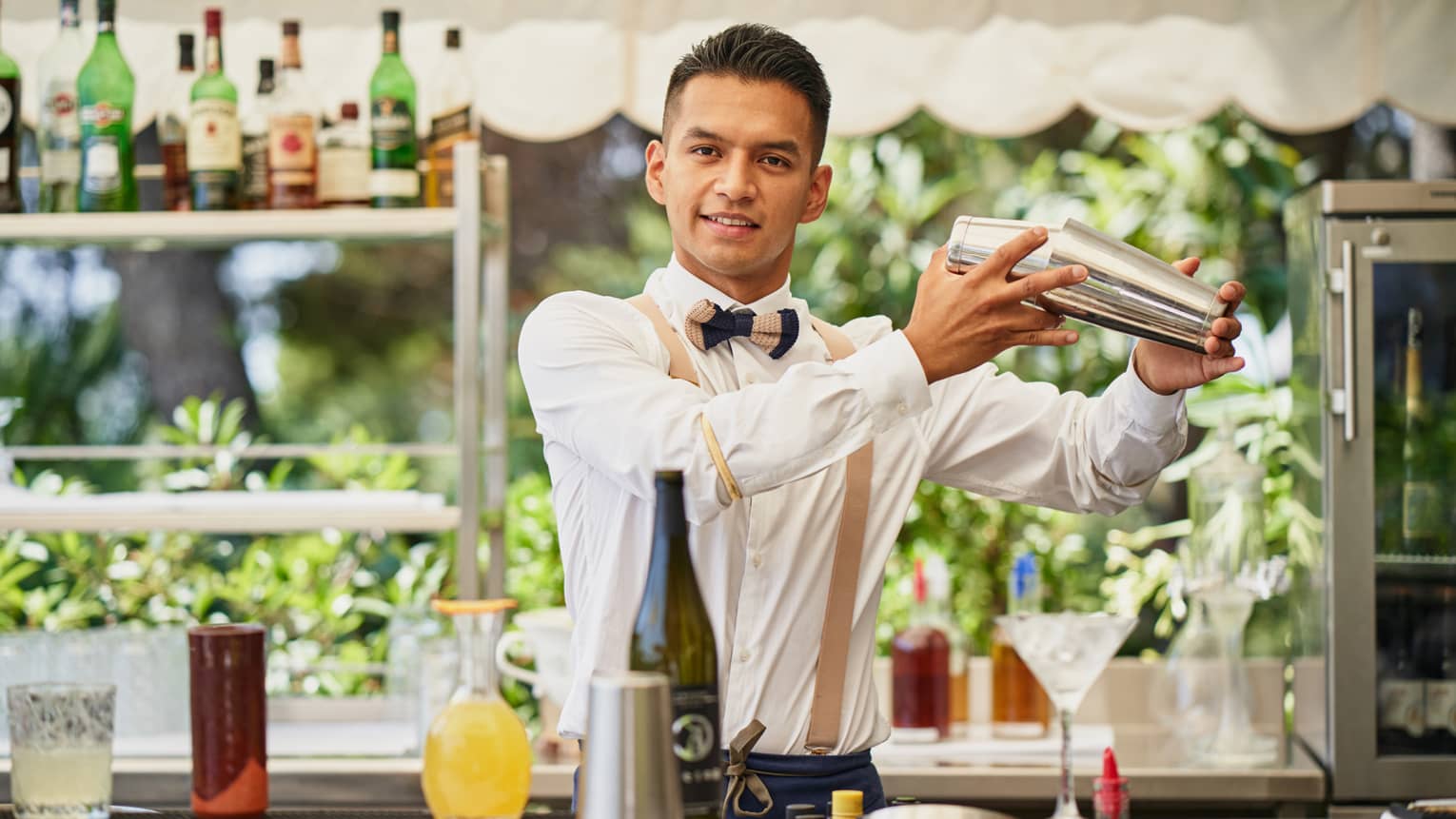 Barman Frank Carcamo standing behind outdoor bar, shaking a cocktail