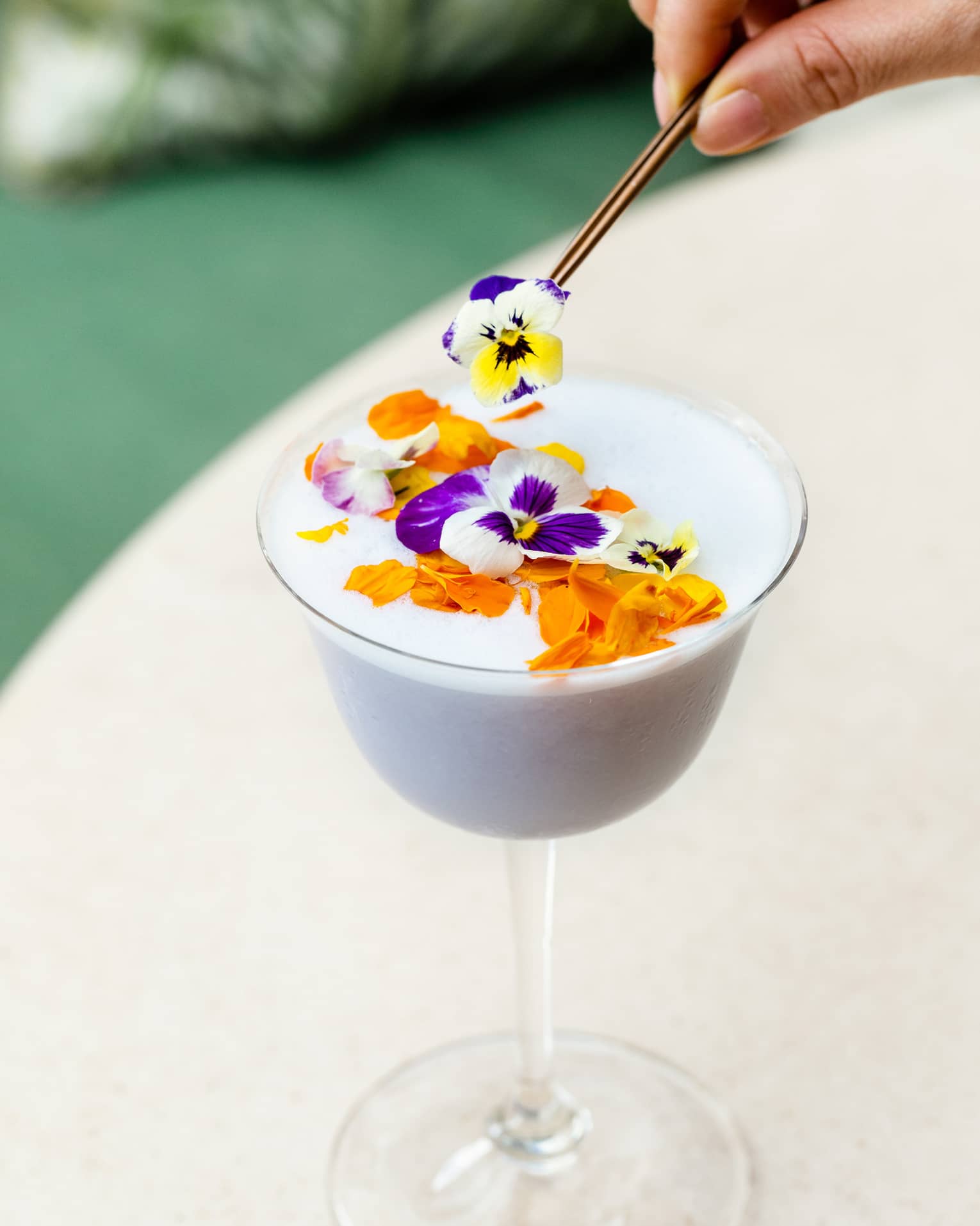 A stemmed glass of a white tropical cocktail topped with flowers