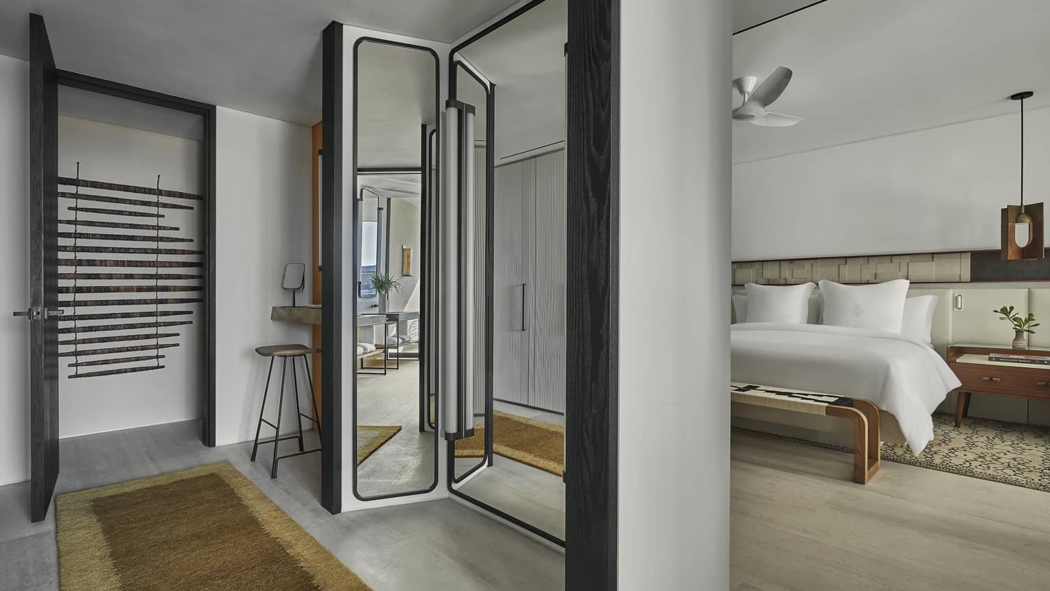 A hotel room with a bed, mirror, bench and small table.